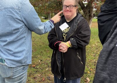 Female camper standing and wearing a black shirt, black jacket, jeans and black glasses smiling for the camera.